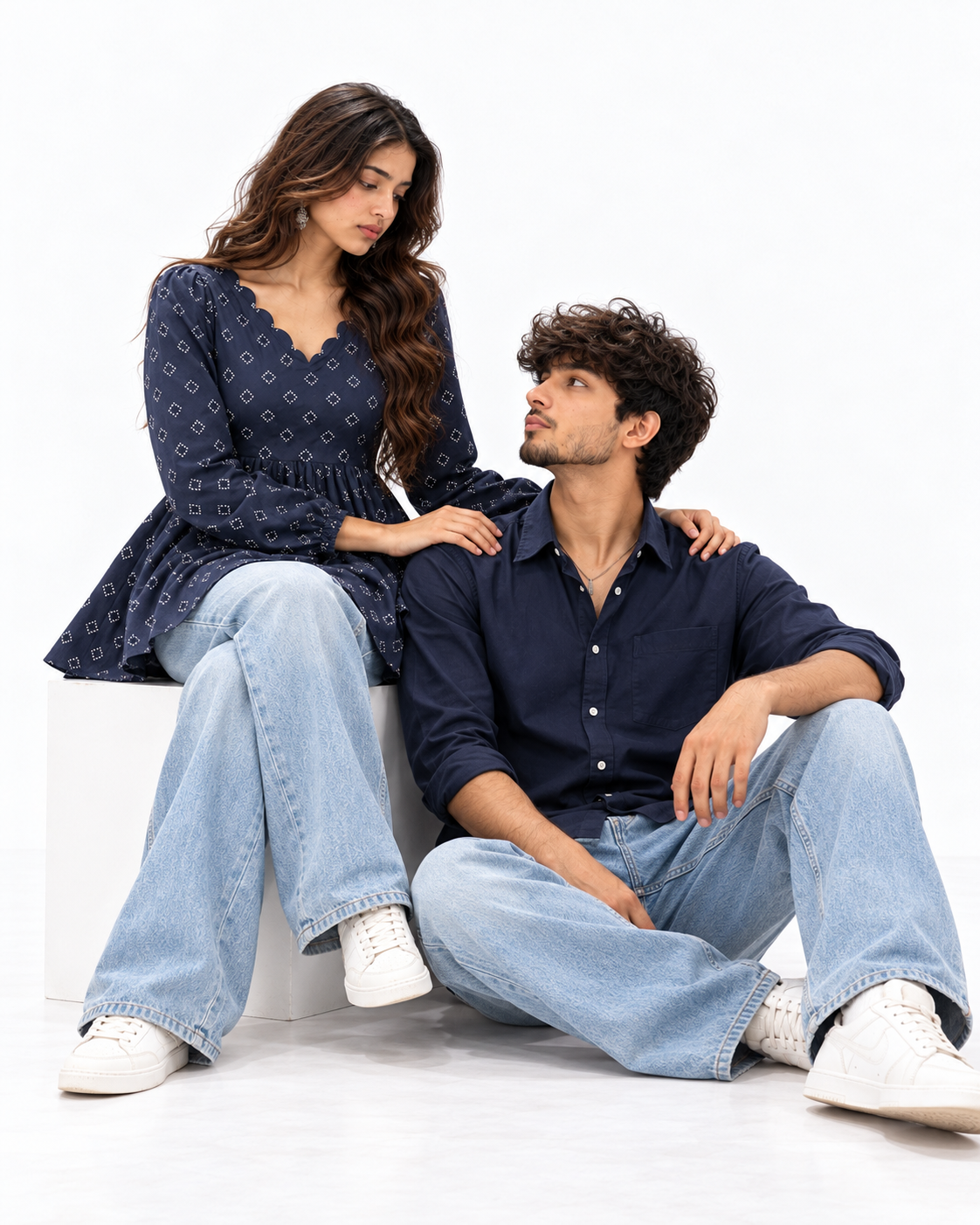 Navy Denim Matching Couple Set - Seated Editorial Studio Pose on White Cube (Kabir & Tara, Tara Seated on Cube, Kabir Seated Beside Cube, Gentle Hand on Shoulder, Unsmiling Poise, Pure White Studio)
